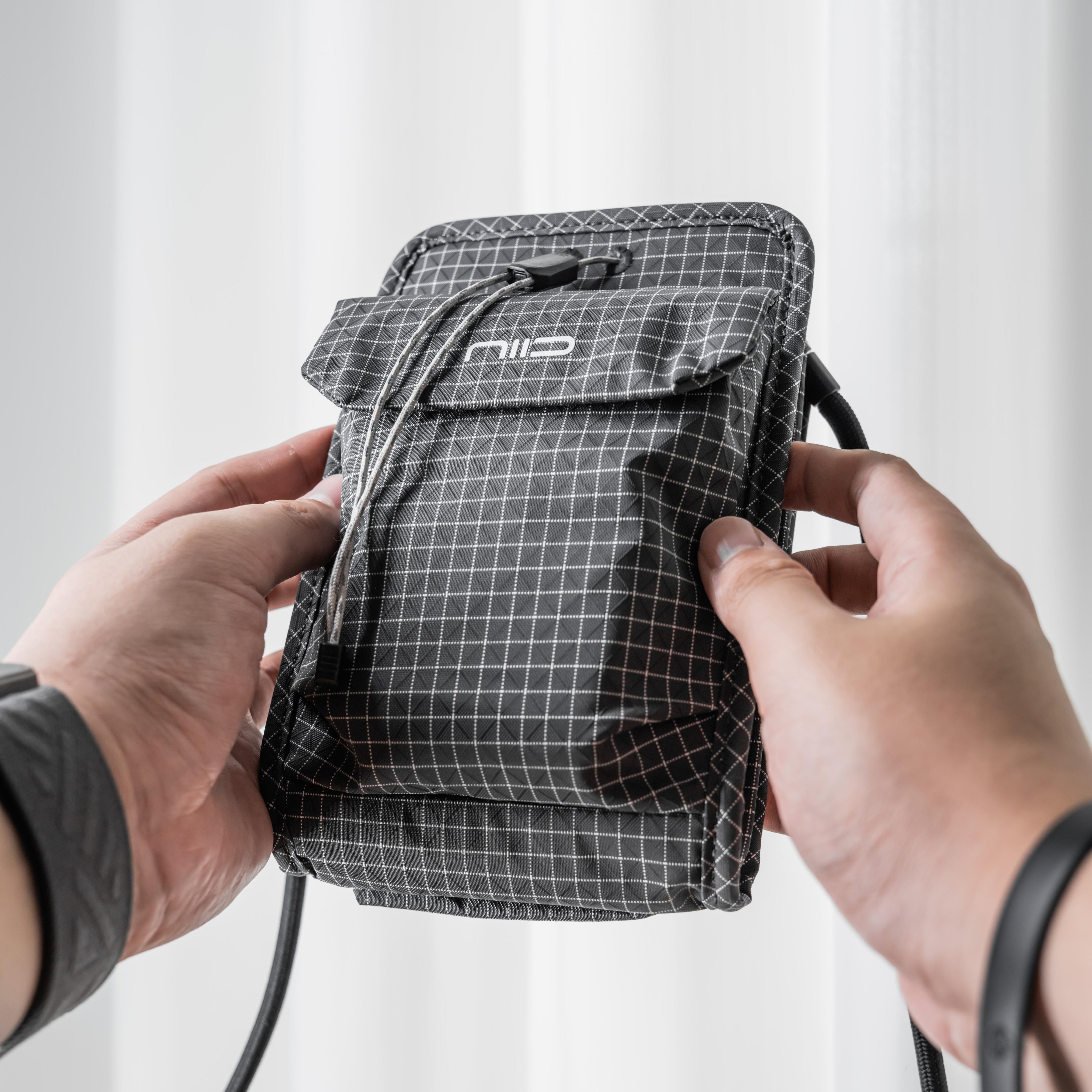 Close-up of hands holding black diamond grid NIID NEO Nomad Pouch, showing NIID logo and magnetic drawstring clasp, lightweight crossbody travel pouch.