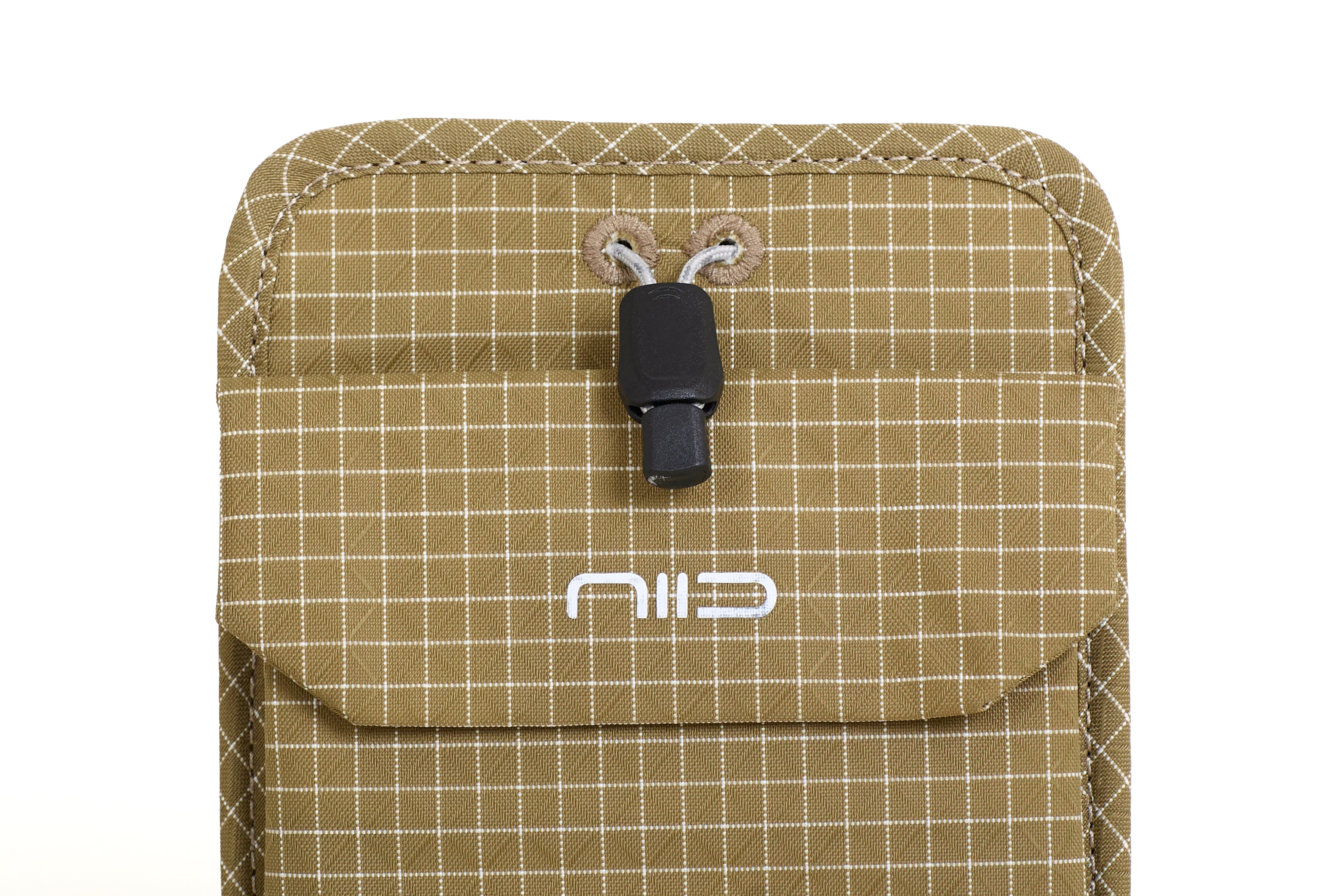 Close-up of Dune Tan Nomad Pouch front flap showing NIID logo, black drawstring cord lock and fabric eyelets.