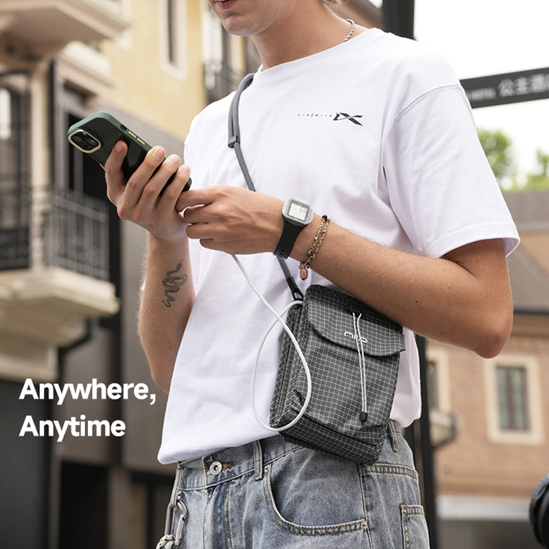 Urban street lifestyle photo of young man in white tee and jeans wearing gray grid NIID NEO Nomad Pouch NP mini crossbody pouch, holding smartphone, city building blurred background, text Anywhere, Anytime daily portable EDC sling bag hero image