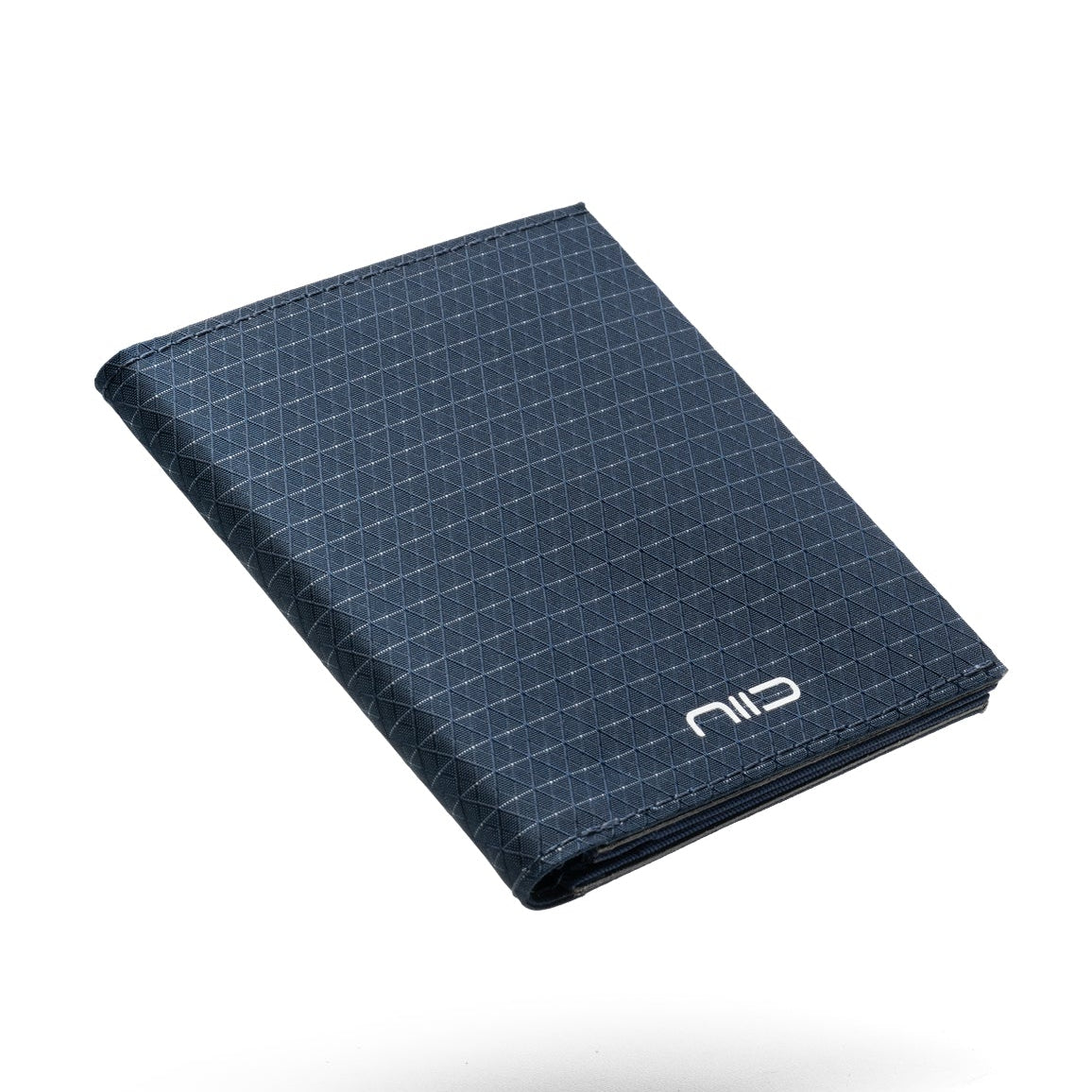 Floating angled shot of dark navy grid Cordura fabric NIID NEX slim bifold wallet on solid clean white background, subtle triangular geometric grid pattern all over surface, white embossed NIID logo on lower front edge, soft shadow underneath, durable lightweight men’s outdoor EDC card holder product photography