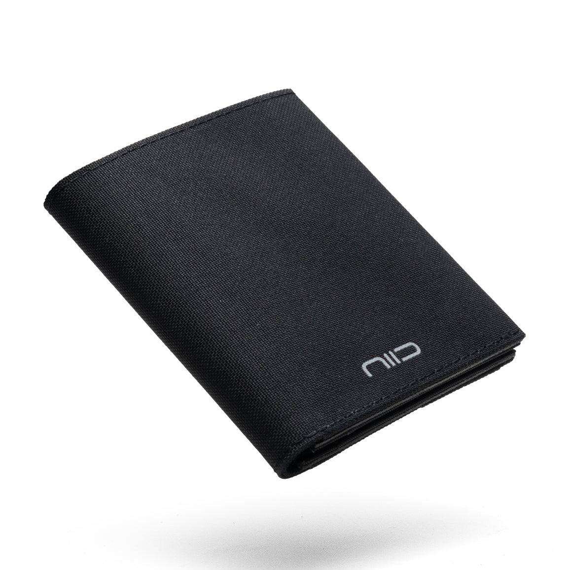 Floating angled shot of solid black smooth Cordura fabric NIID NEX slim bifold wallet on clean solid white background, silver embossed NIID logo on lower front corner, soft subtle shadow underneath, wear-resistant plain fabric minimalist men’s everyday carry card wallet product photography