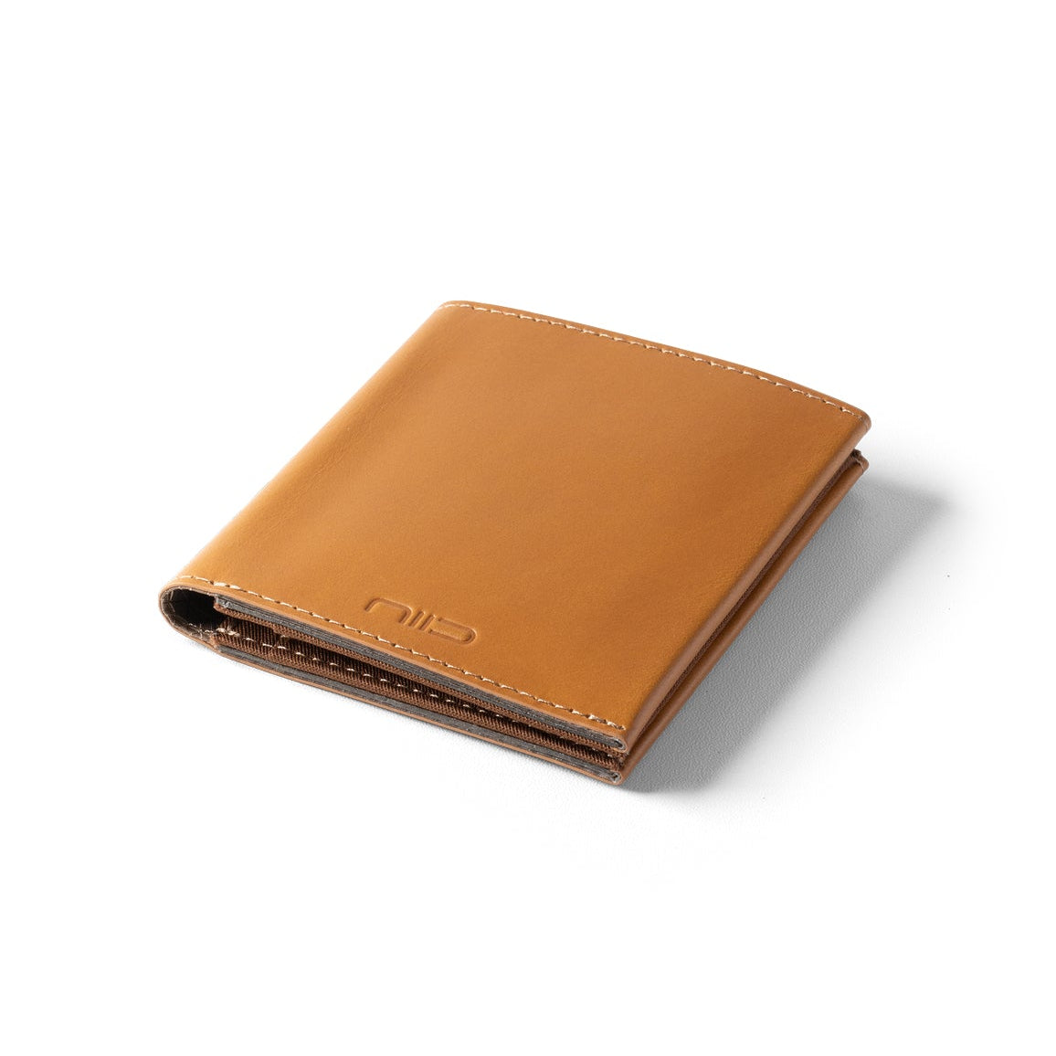 Floating angled shot of tan genuine leather NIID NEX slim bifold wallet on clean solid white background, soft subtle shadow underneath, embossed NIID logo on lower front, smooth vintage leather minimalist men’s front pocket card holder product photography