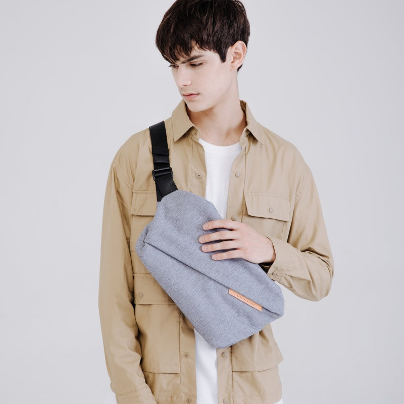 NIID RO Plus light gray crossbody sling bag for men, minimalist urban commute chest bag with adjustable black strap and leather logo tag, casual daily wear model shot