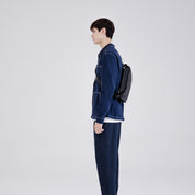 Side profile shot of man in dark denim suit carrying NIID RO Plus meteorite black crossbody sling bag, minimalist urban commute chest pack with adjustable strap, plain light gray studio background