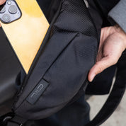 Real‑user hands‑on detail shot for NIID Radiant R2 sling bag Diamond Grid Black, demonstrating side pocket storage capacity with smartphone inside, shows textured grid fabric and embossed NIID logo, reflects daily EDC item‑carrying experience.
