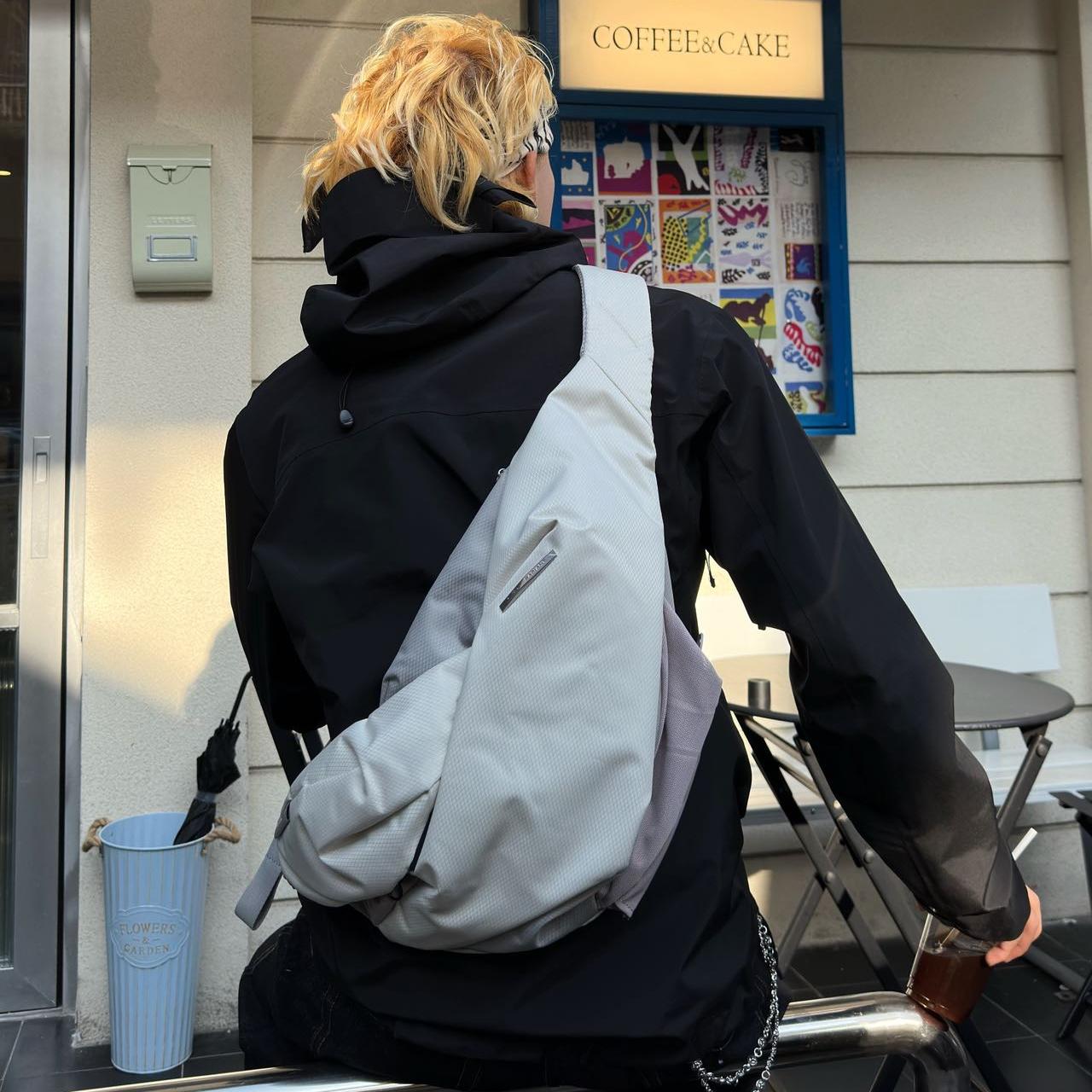 Real‑customer outdoor lifestyle shot of NIID Radiant R2 modular everyday sling bag in Diamond Grid Gray, cross‑back carry beside city coffee shop. Displays practical real‑life silhouette, ideal for urban hangouts, daily commuting and casual city travel.