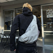 Real‑customer street lifestyle shot of NIID Radiant R2 modular everyday sling bag in Diamond Grid Gray, worn cross‑back outside urban café storefront. Showcases relaxed real‑world carry silhouette for city commute and casual daily outings.