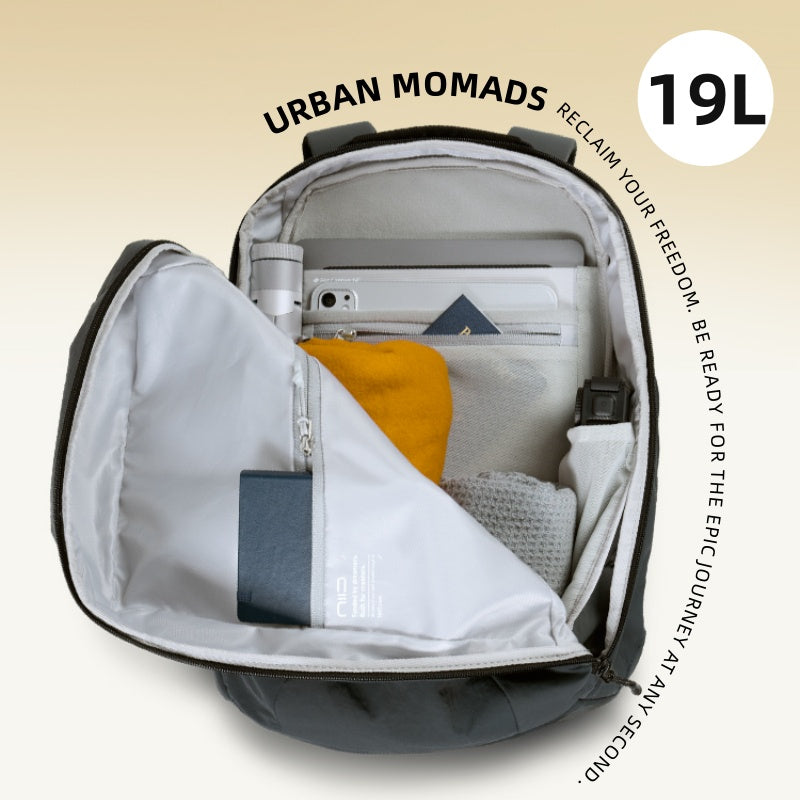  Top-down overhead shot of fully unzipped dark gray NIID Urban Nomads 19L backpack with light gray inner lining, packed with laptop, smartphone, wallet, towel and daily travel accessories; curved surrounding text 