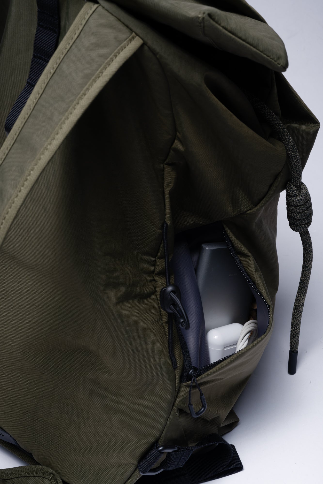 Close-up detail shot of olive green NIID VIA roll-top backpack, featuring secure side zipper pocket that holds chargers and small daily tech gadgets for easy quick access