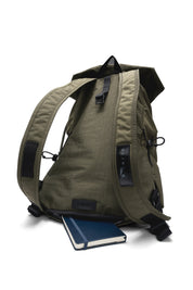 Rear full view of olive green NIID VIA roll-top backpack, displaying wide adjustable padded shoulder straps, brand leather tag and side drawstring pockets, paired with a notebook to show daily office carrying scene