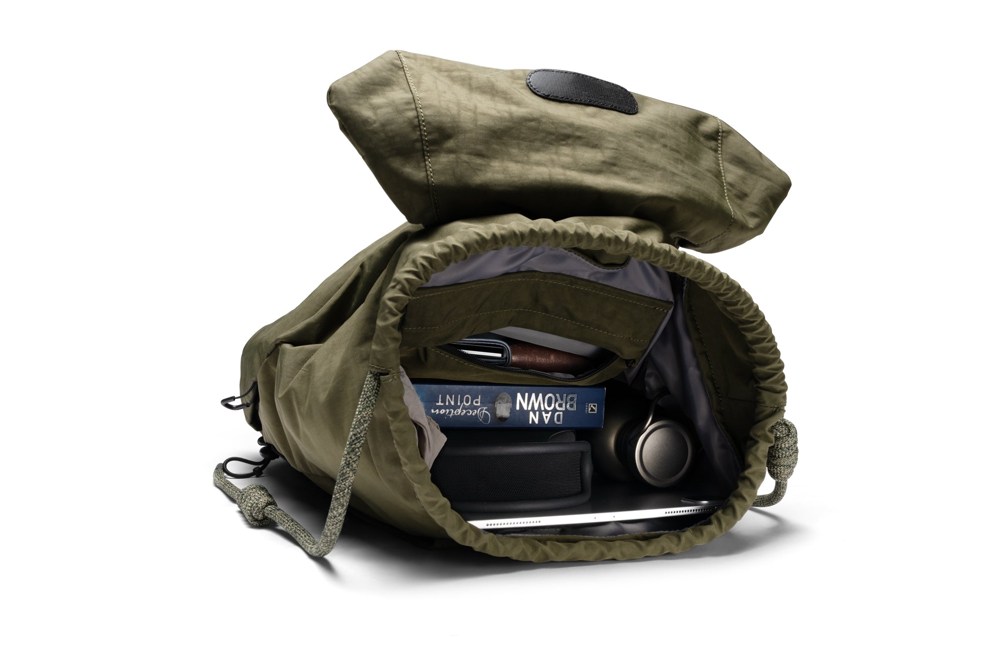 Open olive green NIID VIA roll-top backpack showing roomy inner compartment, fully packed with books, tablet and headphones to demonstrate generous daily storage space