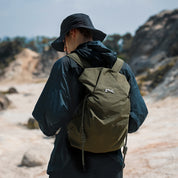 Olive green NIID VIA roll-top backpack worn by a man exploring rocky wilderness, lightweight water-resistant daypack designed for outdoor hiking and casual weekend travels