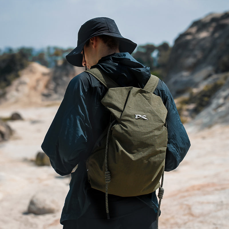 Olive green NIID VIA roll-top backpack worn by a man exploring rocky wilderness, lightweight water-resistant daypack designed for outdoor hiking and casual weekend travels