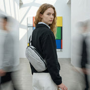 Female model wearing NIID NEO Nomad Sling Bag‑N1L pearly‑grey crossbody bag, modern art corridor background