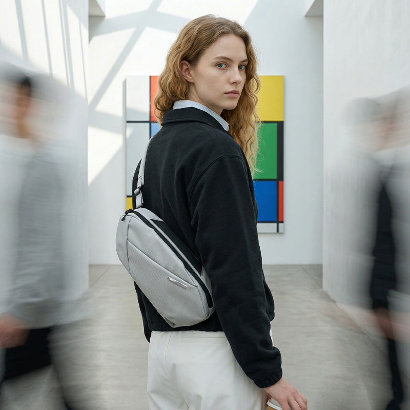 Female model wearing NIID NEO Nomad Sling Bag‑N1L pearly‑grey crossbody bag, modern art corridor background