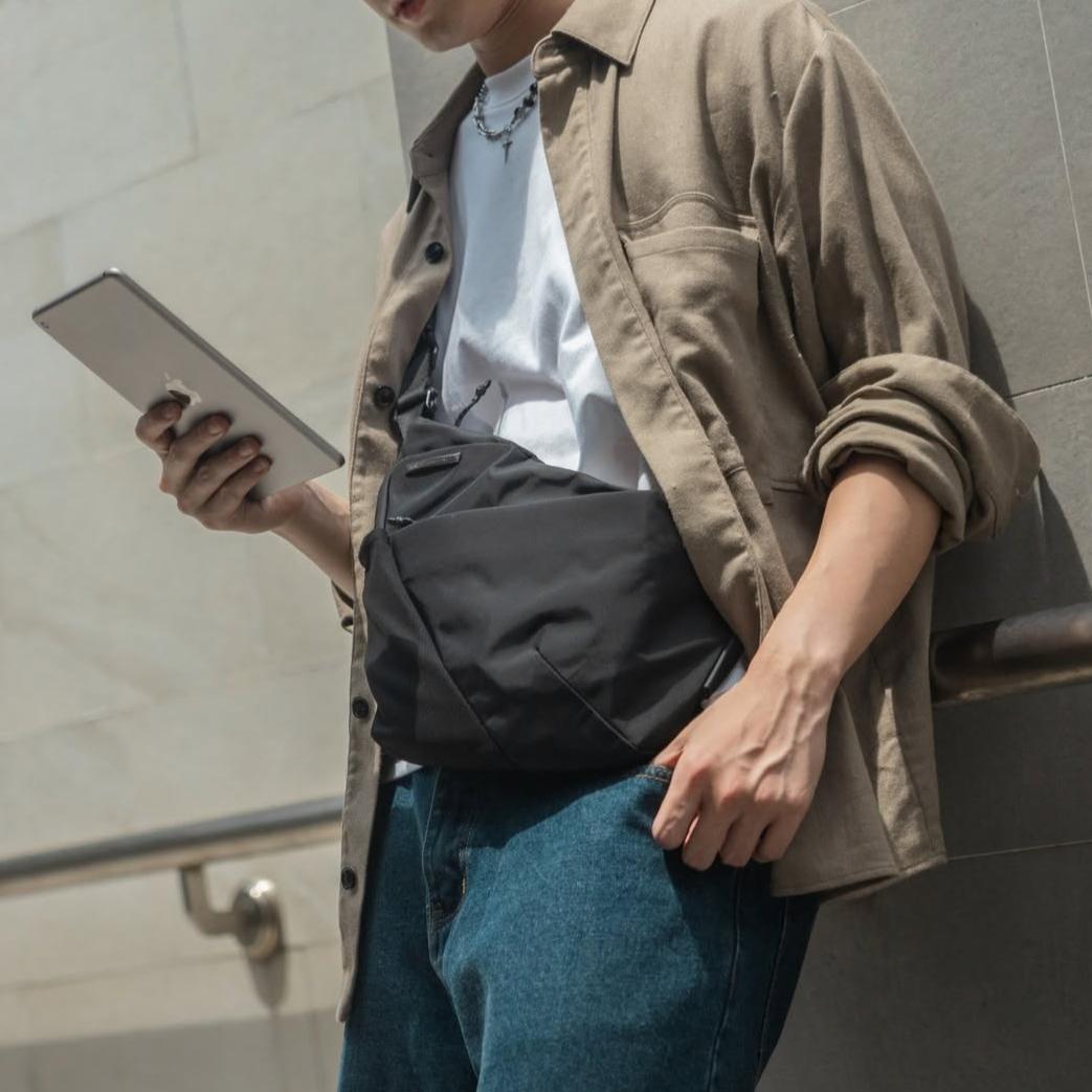 An urban professional using a tablet while wearing the NIID FINO V F5 sling bag close to the chest, showcasing its ergonomic, anti-theft underarm fit designed for secure European travel and city transit.