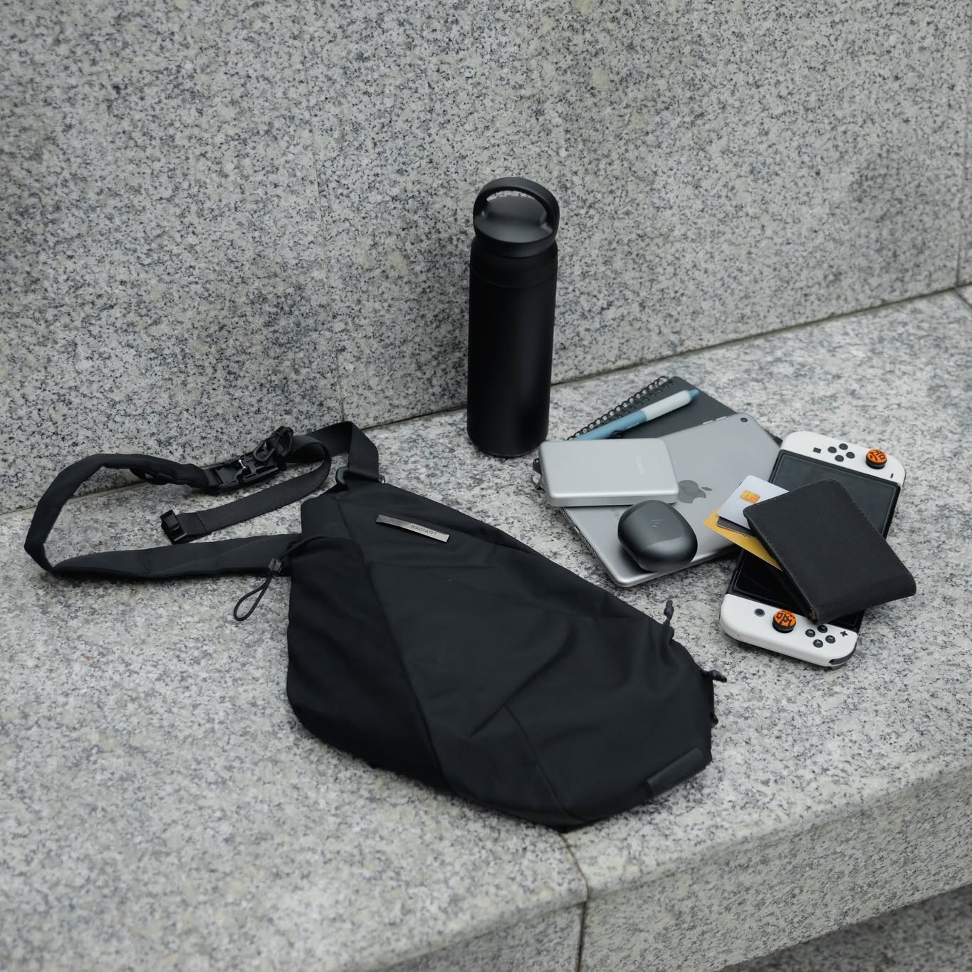 NIID FINO V F5 techwear sling bag showcased with everyday carry tech gear including a tablet, portable console, water bottle, and wireless earbuds, highlighting its premium organization for urban professionals and digital nomads.