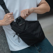 Close-up of the NIID FINO V F5 ergonomic sling bag showing a user retrieving a smartphone from the dedicated quick-access pocket, featuring an integrated smart card slot for ultimate tech mobility.