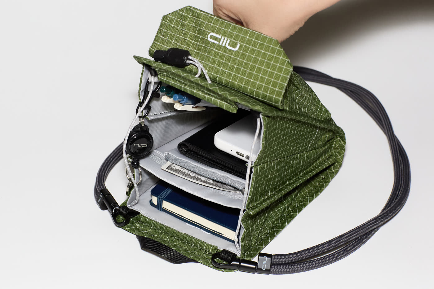 Detailed interior view of the NIID NEO Nomad Pouch in Pine Green, featuring organized slots for a passport, credit cards, pens, and smartphone.