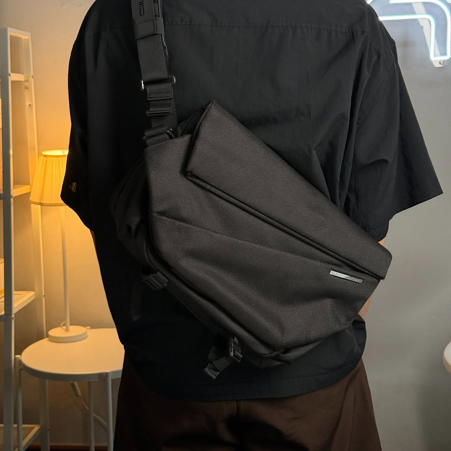 A close-up back view of a tech commuter wearing the NIID Radiant R1 MEGA sling bag in black, showcasing its sleek minimalist profile and premium expandable tech gear storage tailored for digital nomads.