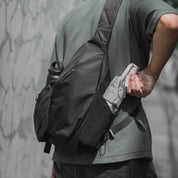NIID Radiant R2 everyday sling bag in charcoal black worn by an urban professional digital nomad, featuring expandable pockets for tech gear and a water bottle.