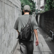 Rear view of an urban professional digital nomad walking through a city street, wearing the sleek, minimalist NIID Radiant R2 modular crossbody sling bag in black.