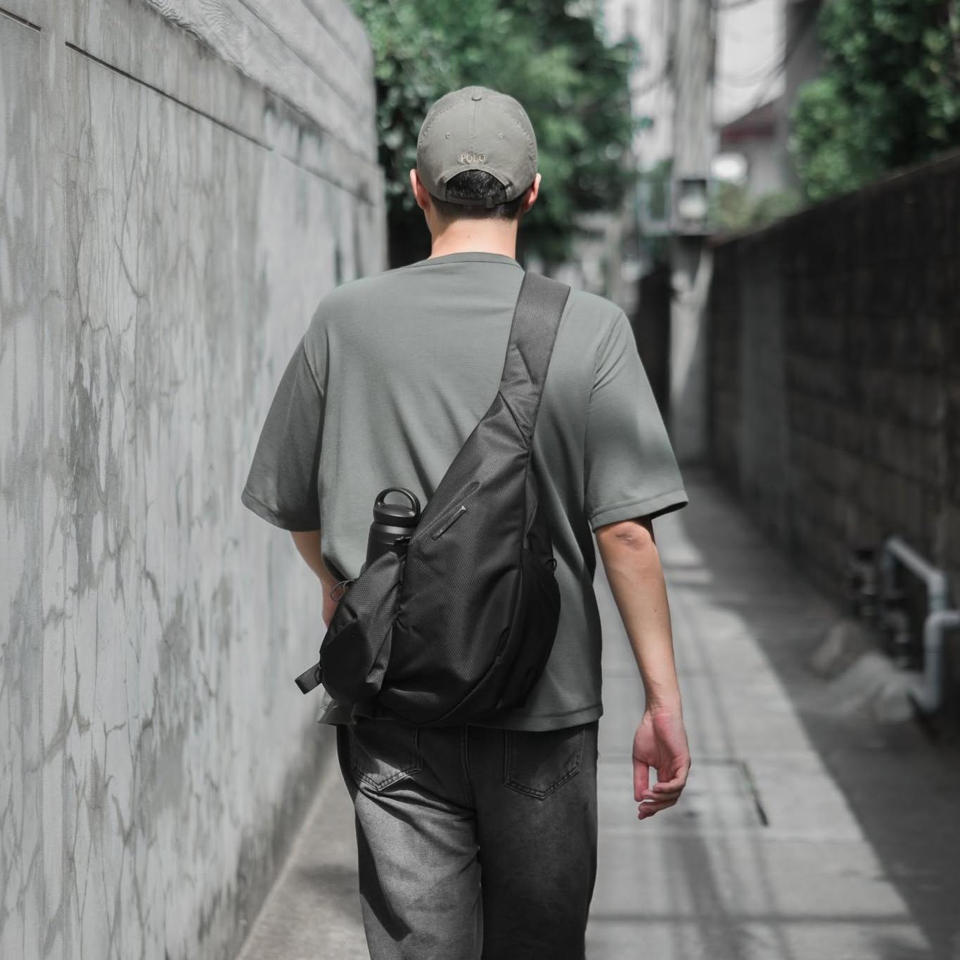 Rear view of an urban professional digital nomad walking through a city street, wearing the sleek, minimalist NIID Radiant R2 modular crossbody sling bag in black.