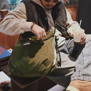 NIID S7 Statement Reversible Tote Bag in Olive and Khaki - Hand Reaching In Indoor Lifestyle Wearing Shot in Café Setting