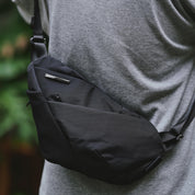 NIID FINO V Ultra‑slim Tech Sling Black Noir worn crossbody over grey t‑shirt, black nylon sling bag outdoor casual torso shot