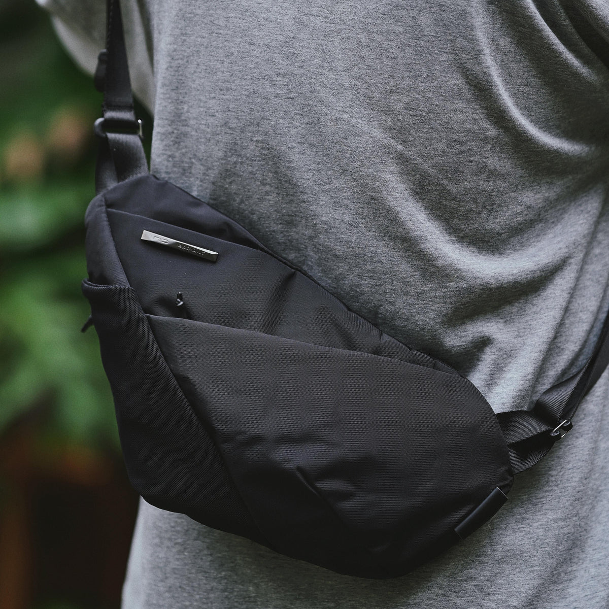 NIID FINO V Ultra‑slim Tech Sling Black Noir worn crossbody over grey t‑shirt, black nylon sling bag outdoor casual torso shot