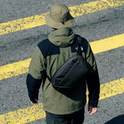 Man viewed from behind wearing bucket hat carrying NIID NEO Nomad 9L Sling Bag‑N2 diamond grid black crossbody sling bag on road street setting
