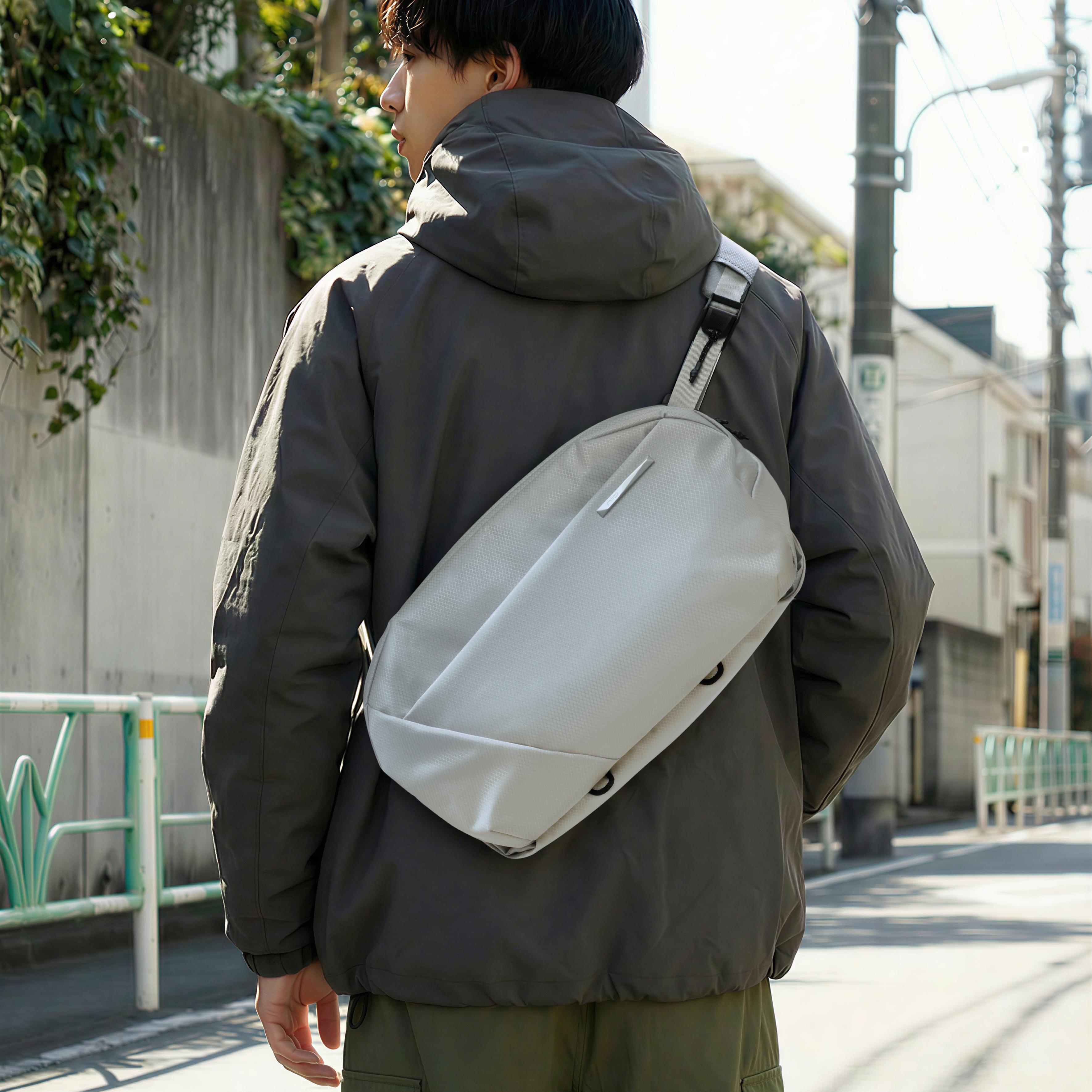 Man viewed from behind carrying NIID NEO Nomad 9L Sling Bag‑N2 pearly gray crossbody sling bag on shoulder, urban street outdoor setting