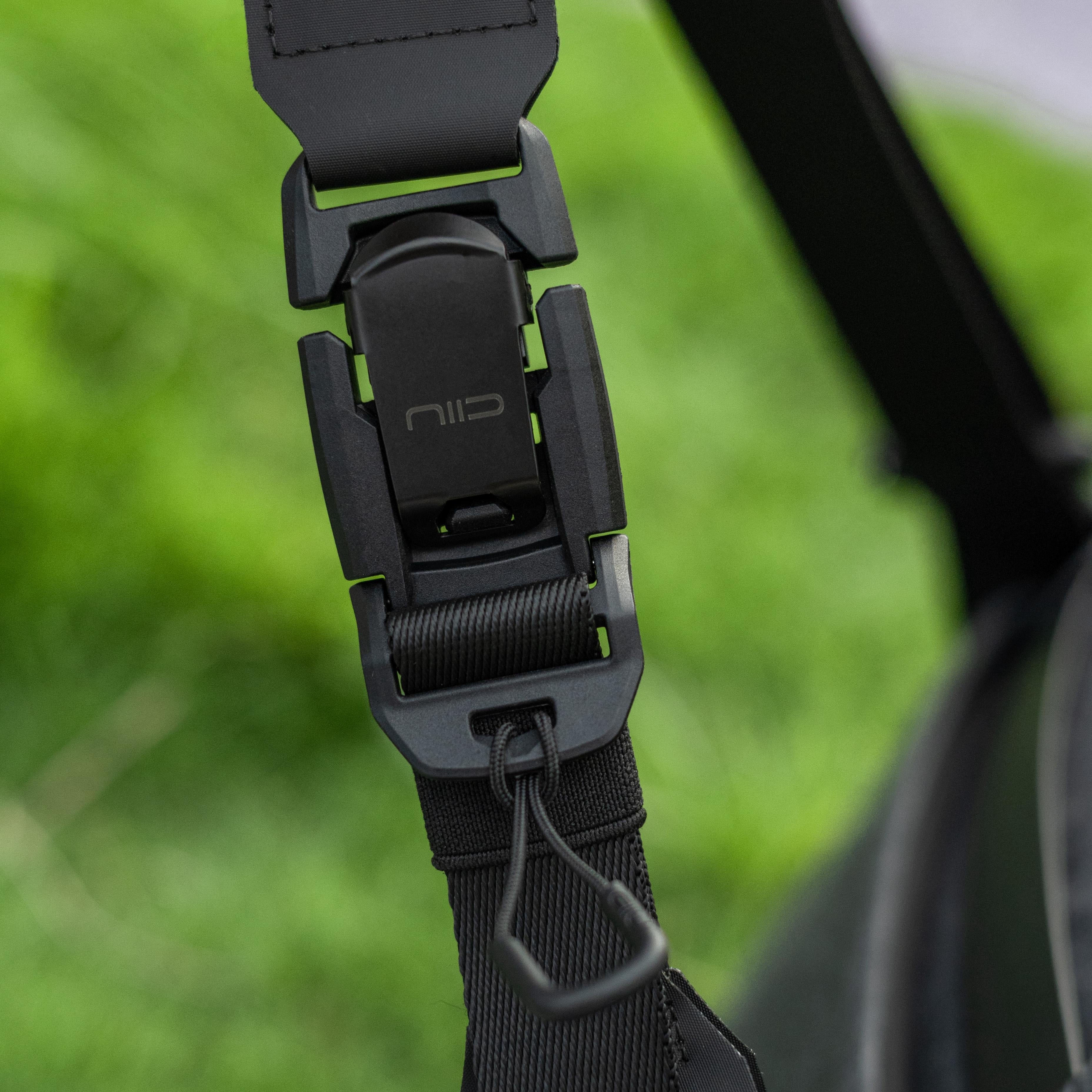Close‑up view of NIID R1 Radiant Mega quick‑release plastic buckle and adjustable shoulder strap with NIID logo, blurred green outdoor background