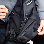 Close‑up shot showing hands manipulating zipper and keychain hardware on NIID Radiant R2 Everyday Sling Bag, black mesh modular crossbody bag interior feature view