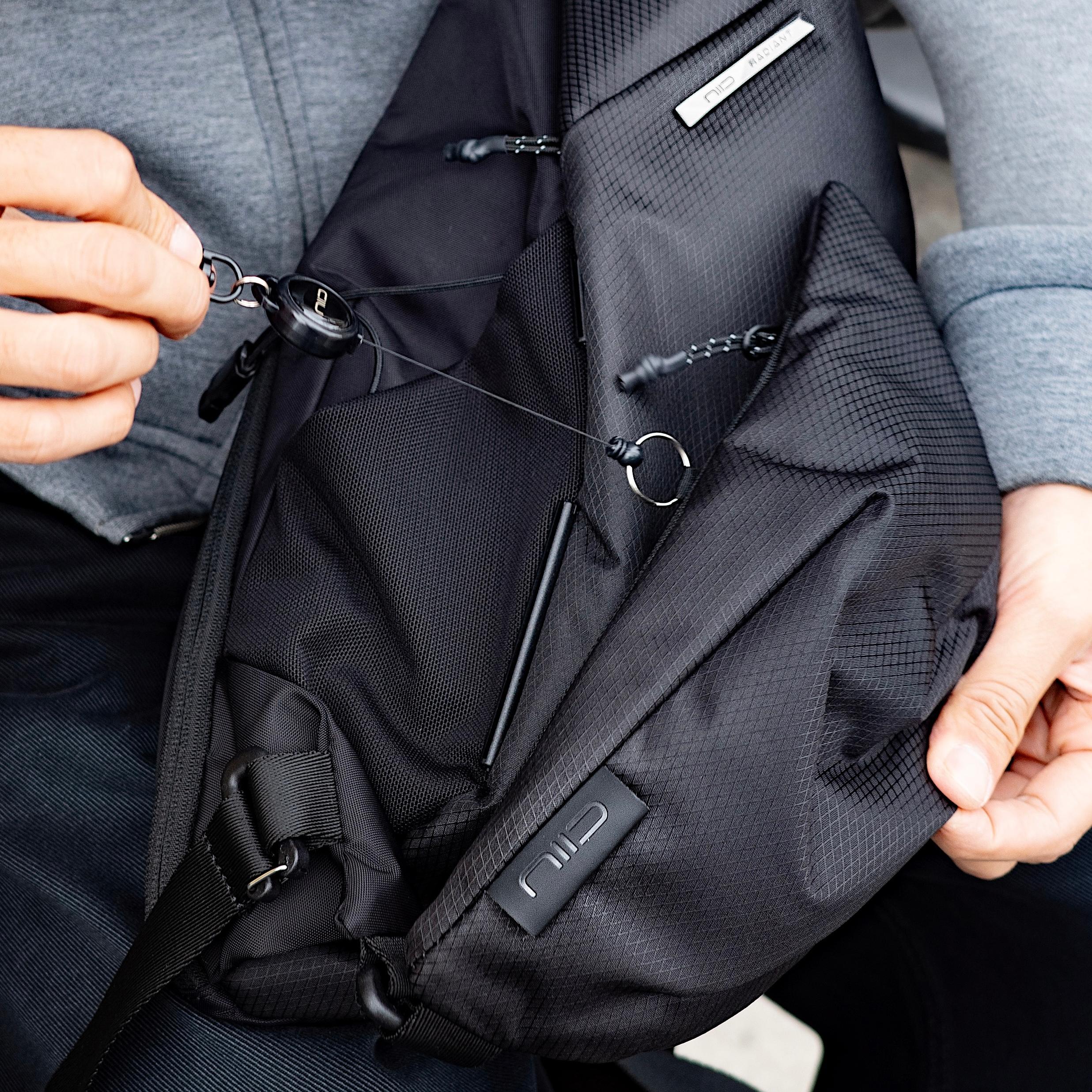 Close‑up shot showing hands manipulating zipper and keychain hardware on NIID Radiant R2 Everyday Sling Bag, black mesh modular crossbody bag interior feature view