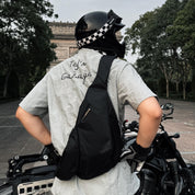 Man wearing motorcycle helmet carrying NIID Radiant R2 Everyday Sling Bag, black modular crossbody bag beside cruiser motorbike on city street for daily commute