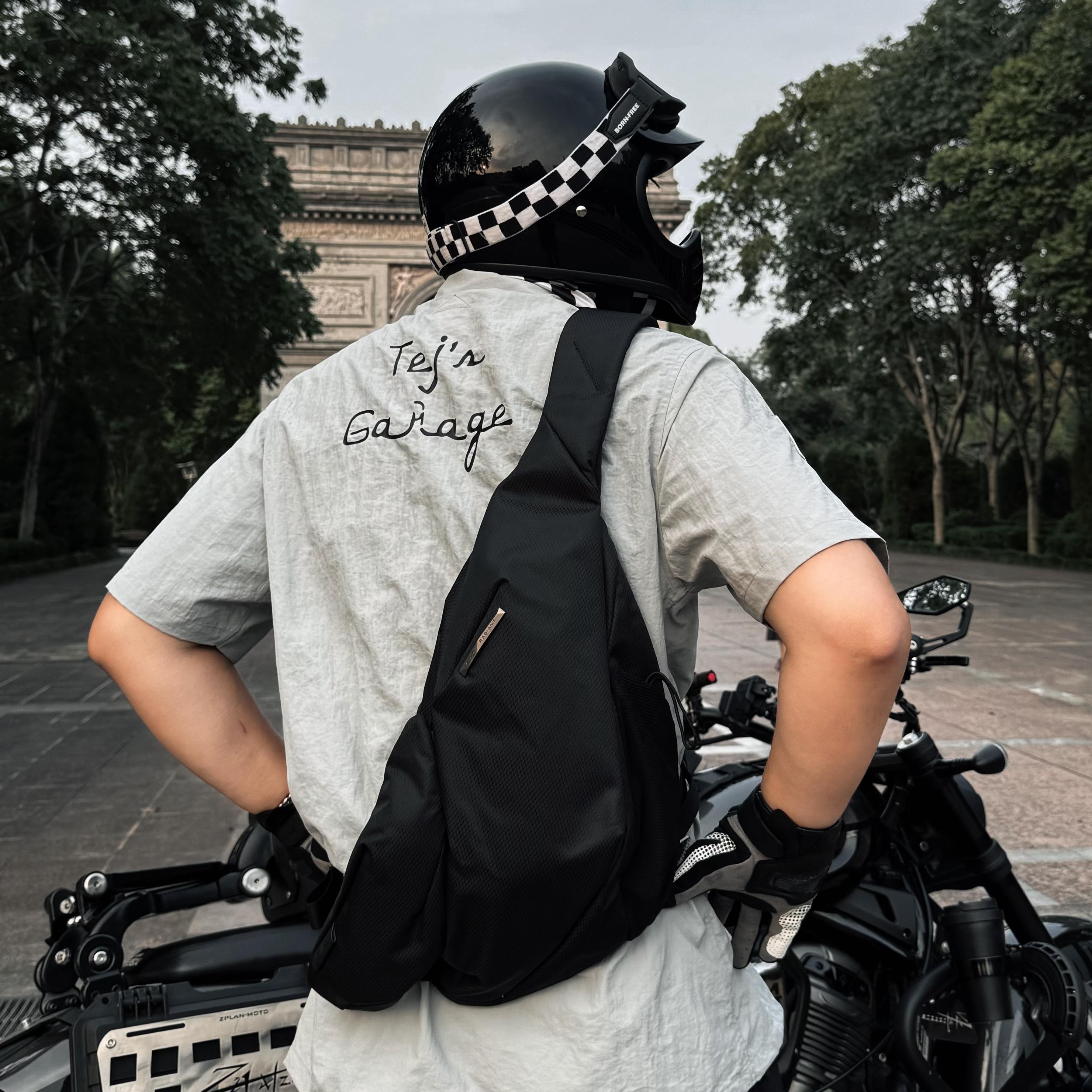 Man wearing motorcycle helmet carrying NIID Radiant R2 Everyday Sling Bag, black modular crossbody bag beside cruiser motorbike on city street for daily commute