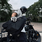 NIID Radiant R2 Everyday Sling Bag, real user shot, man with motorcycle helmet holding black sling bag next to cruiser motorcycle, outdoor daily‑use scene