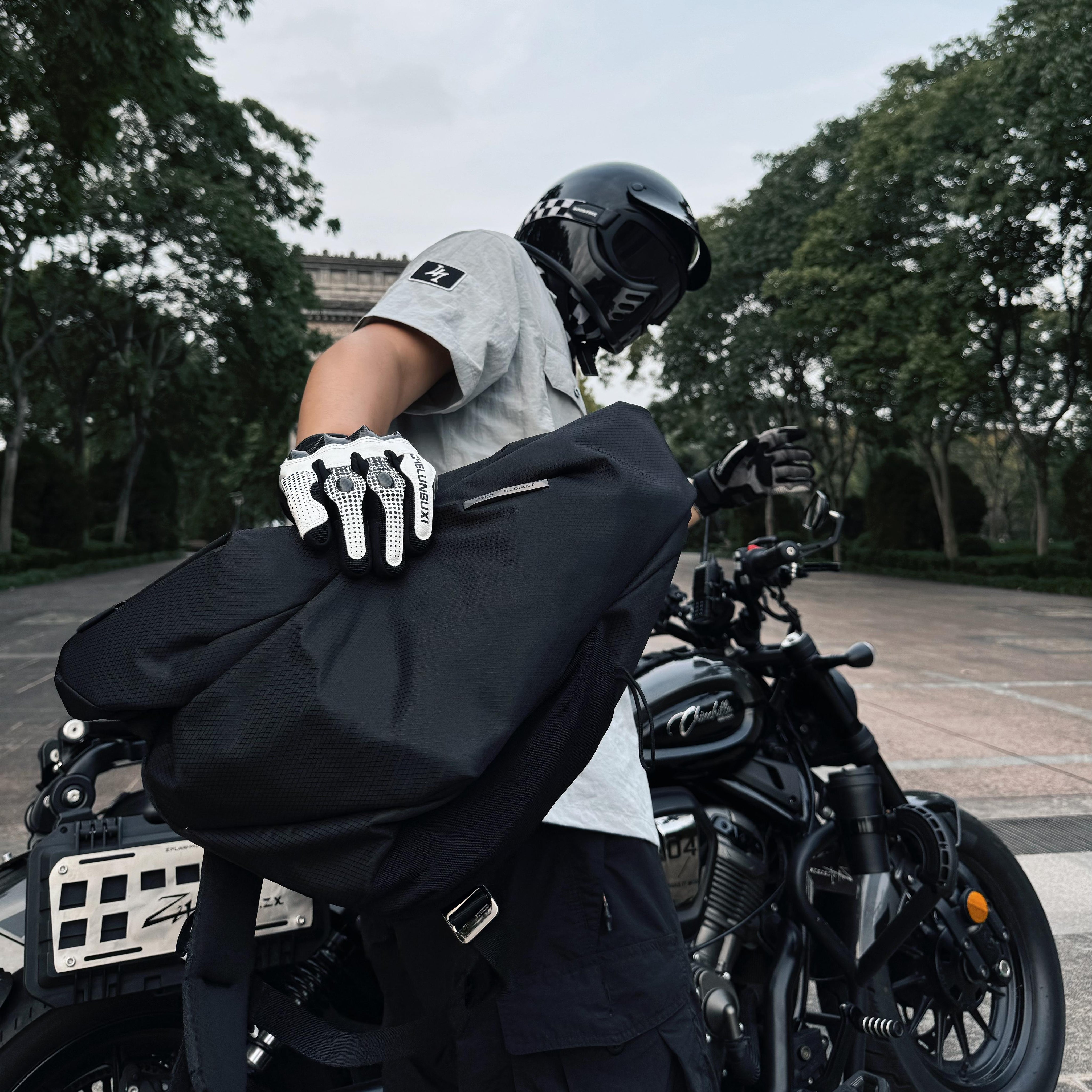 NIID Radiant R2 Everyday Sling Bag, real user shot, man with motorcycle helmet holding black sling bag next to cruiser motorcycle, outdoor daily‑use scene