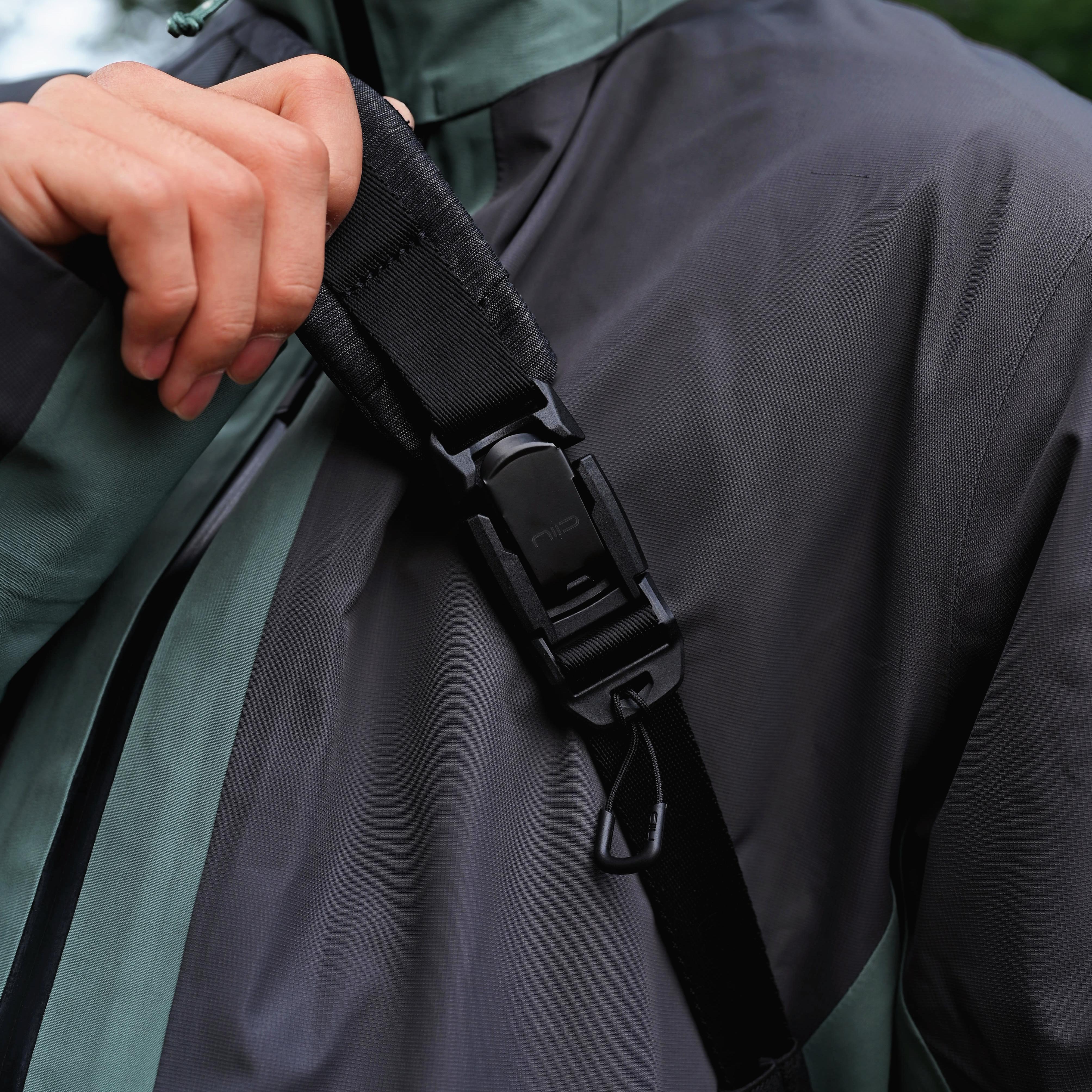 Close‑up of hand gripping the quick‑release buckle strap on NIID Radiant R2 Everyday Sling Bag, showing durable hardware detail with casual outdoor outfit